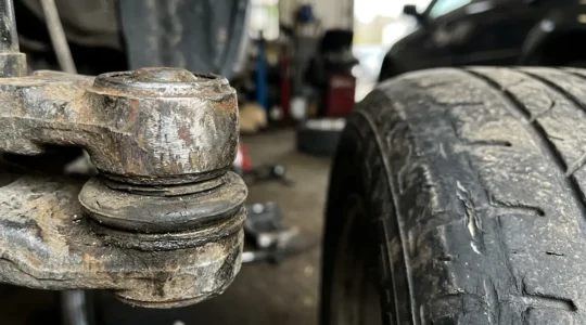 Gros plan sur une rotule de direction usée avec un pneu montrant une usure anormale sur les flancs